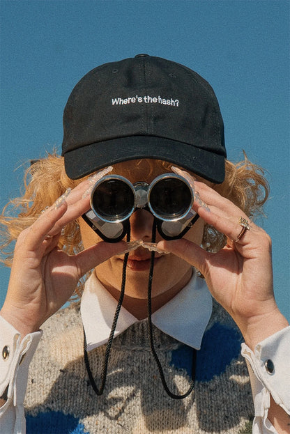 Puffco "Where's the hash?" black washed cotton strapback cap with white embroidery, worn by a person looking through binoculars.