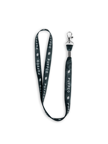 Black Puffco lanyard with white branding, a subtle tie-dye pattern, and a silver metal clasp.